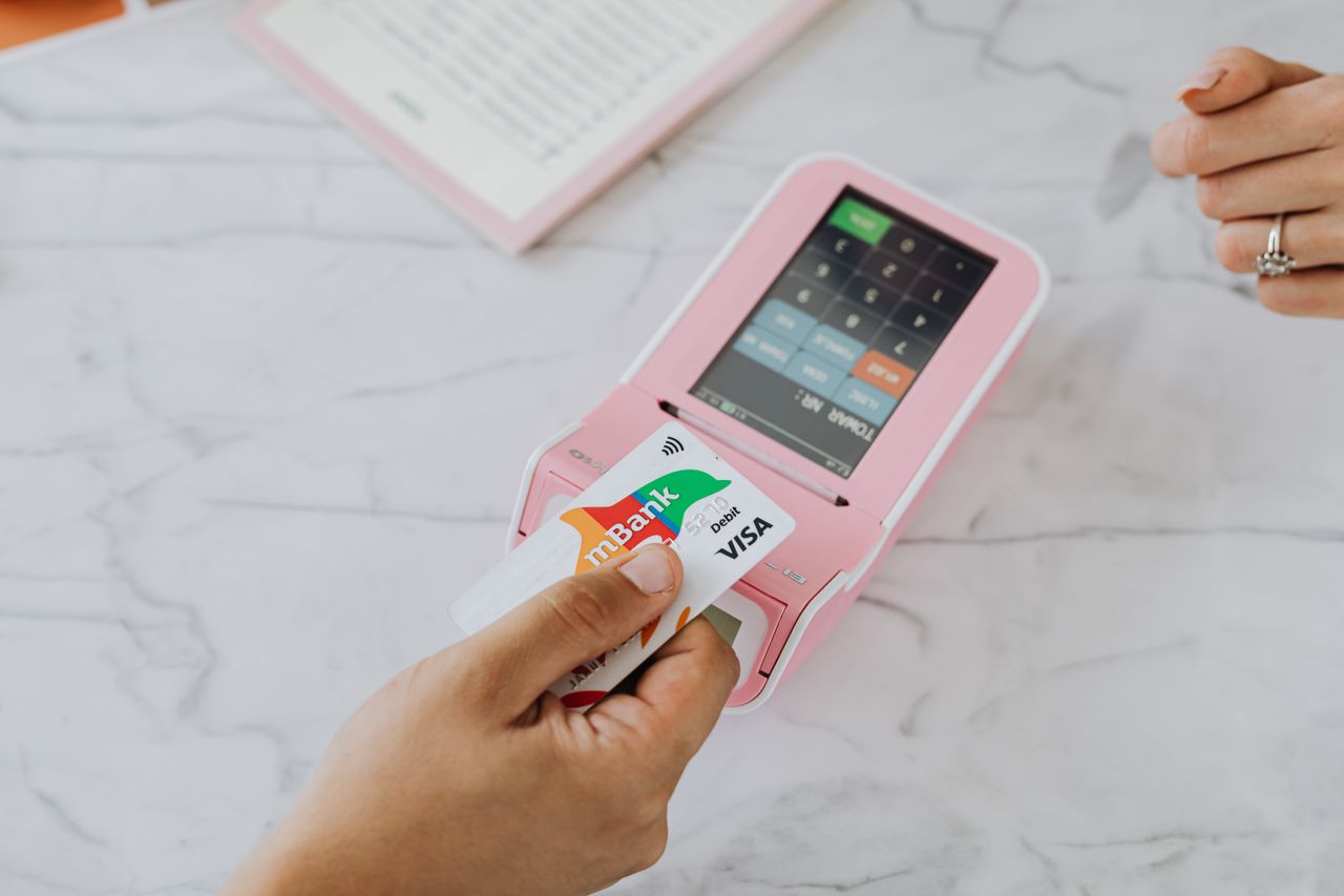 hero-img-02 Hand using a contactless card on a pink POS terminal for a wireless transaction.